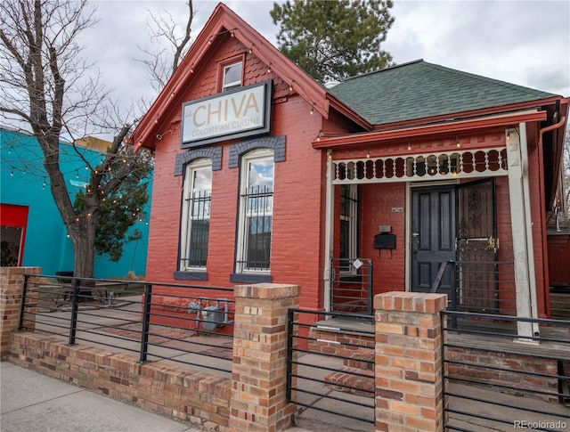 view of front of home with brick siding, a shingled roof, and fence