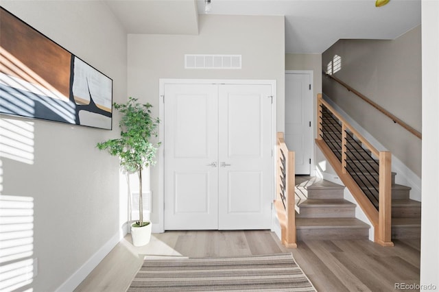 foyer entrance featuring baseboards, wood finished floors, visible vents, and stairway