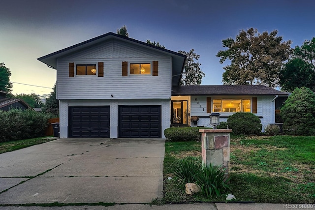 tri-level home featuring brick siding, a garage, concrete driveway, a lawn, and covered porch