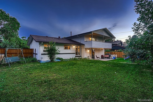 back of house with fence, brick siding, a patio area, a balcony, and a yard