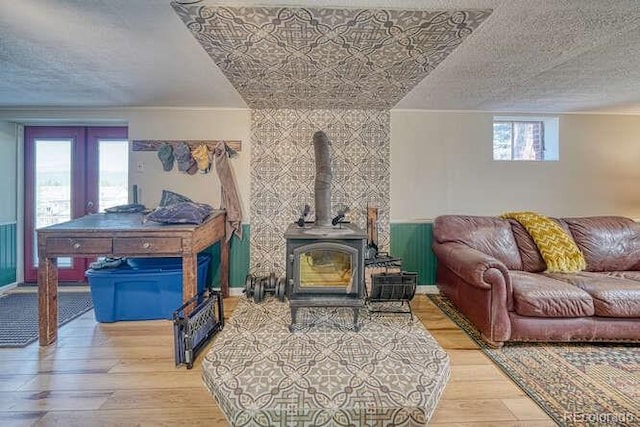 living room with a textured ceiling, light hardwood / wood-style flooring, a wood stove, and french doors