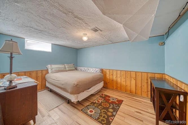 bedroom featuring a textured ceiling, light hardwood / wood-style floors, and wooden walls