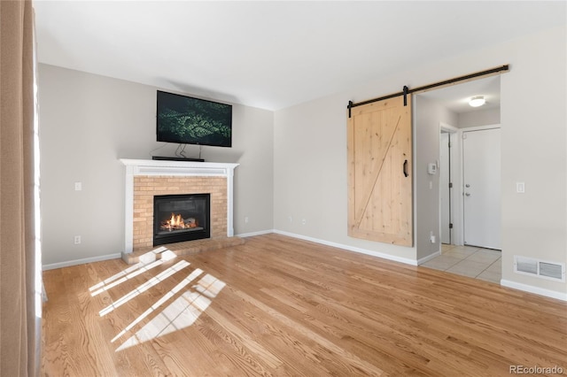 9898 Tourmaline Ct, Parker, CO 80134 - unfurnished living room with light wood-type flooring, a barn door, a brick fireplace, and baseboards
