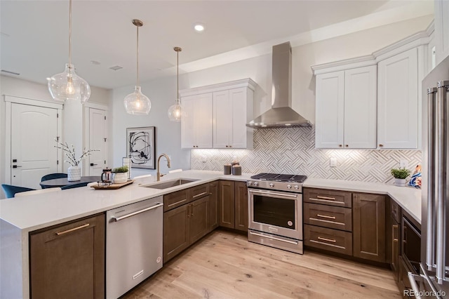 kitchen with pendant lighting, wall chimney range hood, decorative backsplash, appliances with stainless steel finishes, and white cabinetry