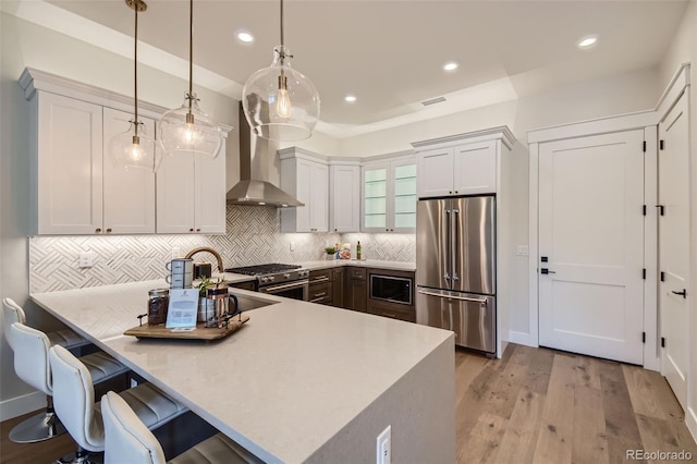 kitchen with wall chimney exhaust hood, premium appliances, white cabinetry, and decorative light fixtures