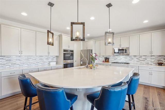 kitchen featuring white cabinetry, an island with sink, appliances with stainless steel finishes, and decorative light fixtures