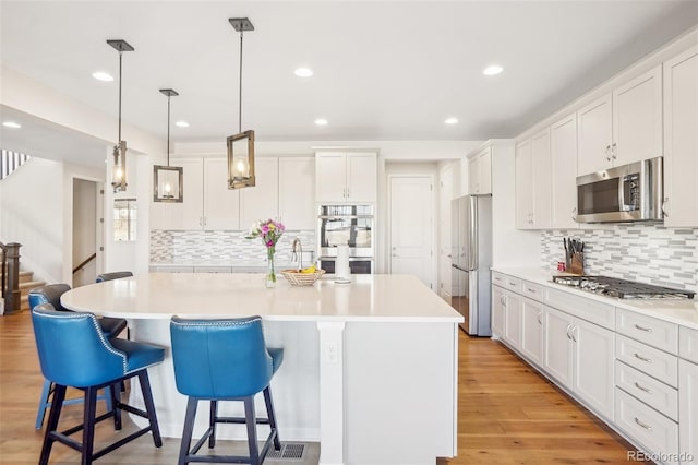 kitchen with white cabinetry, appliances with stainless steel finishes, pendant lighting, and a center island with sink