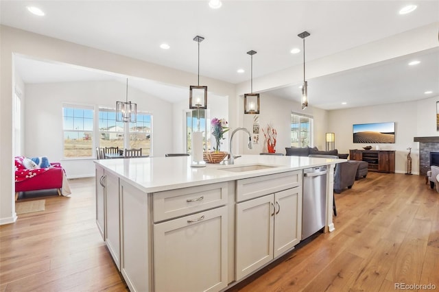 kitchen featuring pendant lighting, sink, a kitchen island with sink, stainless steel dishwasher, and light hardwood / wood-style flooring