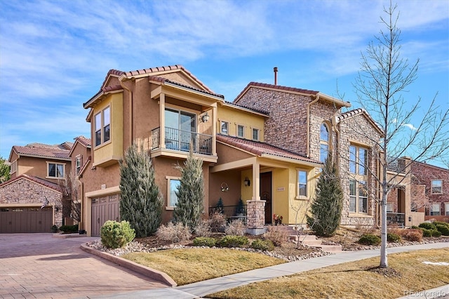 mediterranean / spanish-style home featuring a balcony, stone siding, decorative driveway, and stucco siding