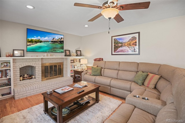 living room featuring ceiling fan, light hardwood / wood-style floors, and a brick fireplace