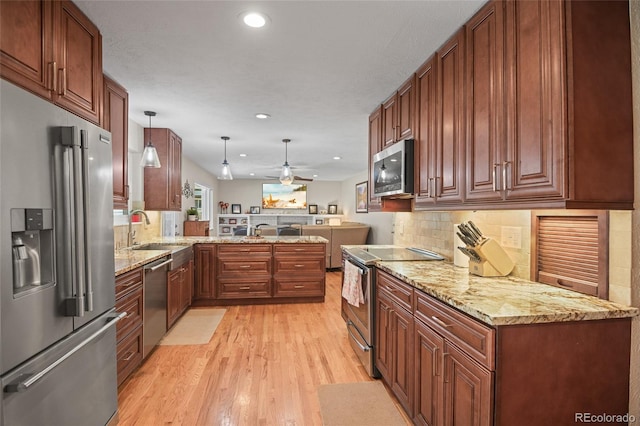 kitchen with sink, stainless steel appliances, kitchen peninsula, light hardwood / wood-style floors, and decorative light fixtures