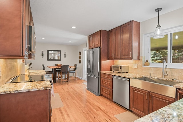 kitchen with appliances with stainless steel finishes, tasteful backsplash, sink, decorative light fixtures, and light hardwood / wood-style floors