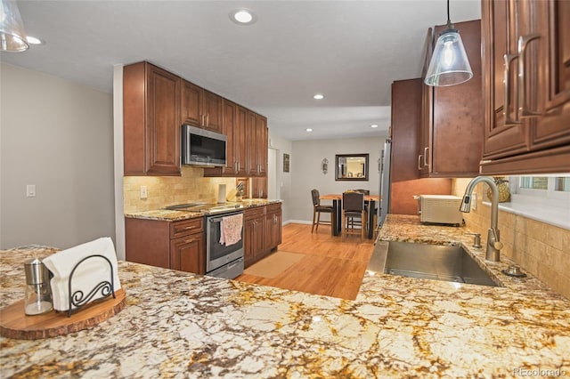 kitchen featuring sink, stainless steel appliances, light hardwood / wood-style flooring, pendant lighting, and decorative backsplash