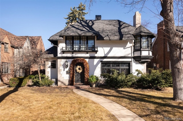 tudor-style house featuring a front lawn, a balcony, and stucco siding