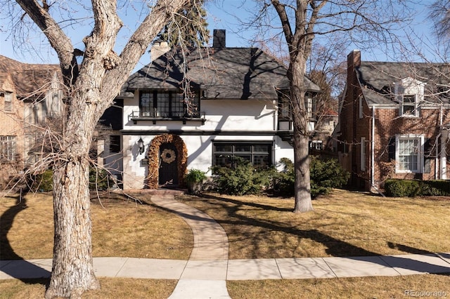 english style home with a front yard, a balcony, and stucco siding