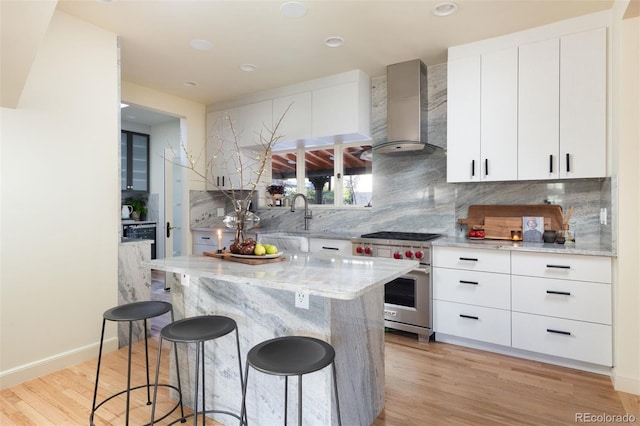 kitchen with tasteful backsplash, light wood-style flooring, a breakfast bar area, luxury range, and wall chimney range hood