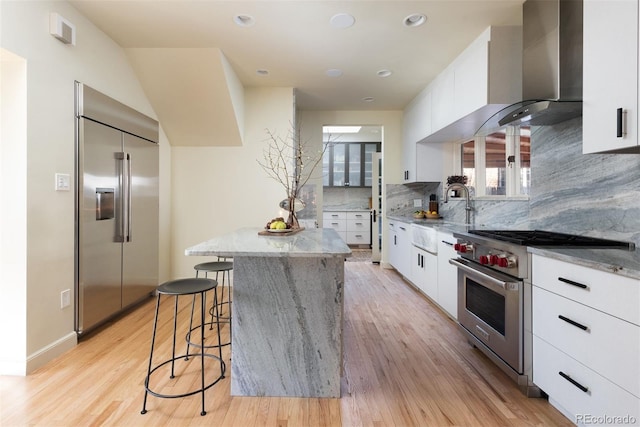 kitchen featuring high end appliances, tasteful backsplash, white cabinetry, a kitchen island, and wall chimney exhaust hood