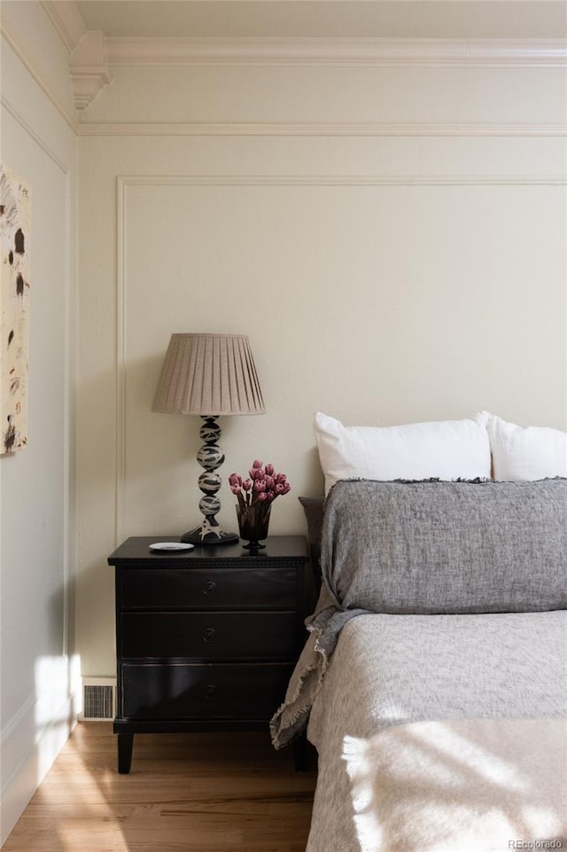 bedroom featuring ornamental molding, visible vents, and wood finished floors