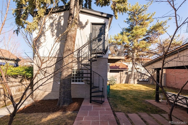 view of property exterior featuring stucco siding, a yard, brick siding, and stairs