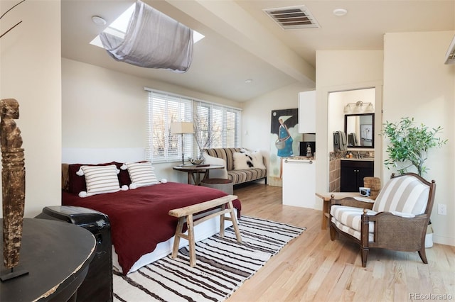 bedroom featuring vaulted ceiling with skylight, visible vents, light wood-style flooring, and connected bathroom