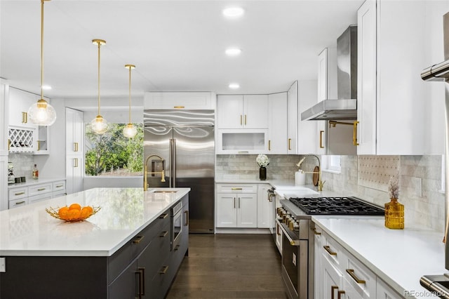 kitchen featuring wall chimney range hood, white cabinets, built in appliances, dark hardwood / wood-style floors, and a kitchen island with sink