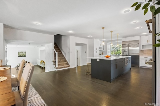 kitchen featuring white cabinets, a center island with sink, dark hardwood / wood-style floors, built in fridge, and decorative light fixtures