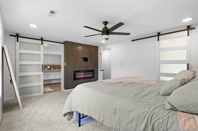 carpeted bedroom with a barn door, a fireplace, ensuite bathroom, and ceiling fan