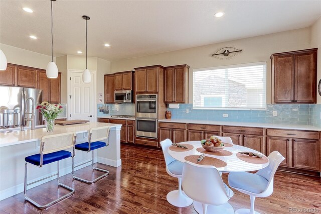 kitchen featuring dark hardwood / wood-style flooring, backsplash, stainless steel appliances, and hanging light fixtures