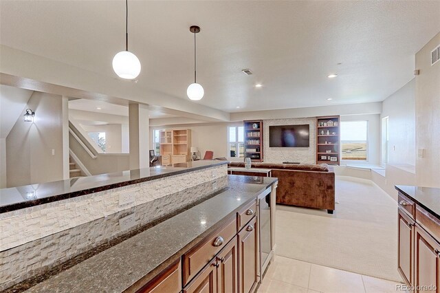 kitchen with a textured ceiling, pendant lighting, light carpet, built in shelves, and dark stone counters