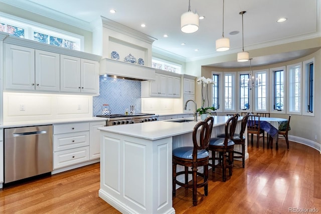 kitchen with a kitchen island with sink, hanging light fixtures, stainless steel dishwasher, and sink