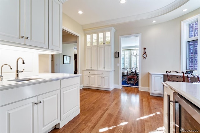 kitchen featuring sink, white cabinetry, crown molding, light hardwood / wood-style flooring, and beverage cooler