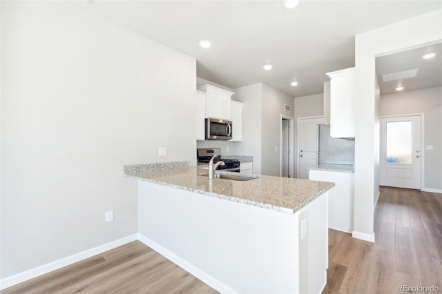 kitchen featuring light stone countertops, stainless steel appliances, kitchen peninsula, light hardwood / wood-style floors, and white cabinets