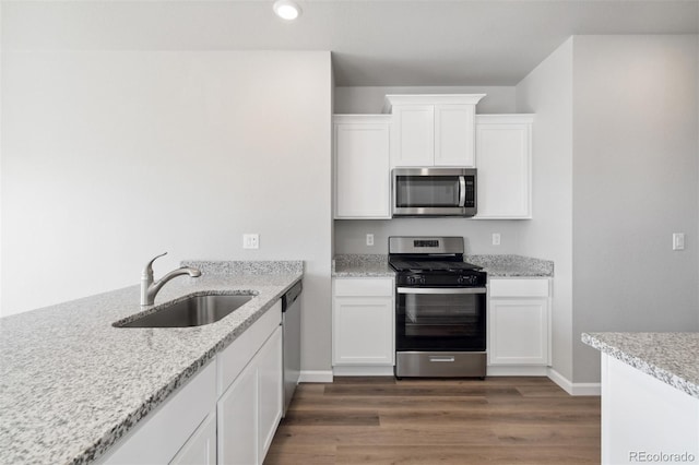 kitchen with light stone countertops, white cabinetry, sink, dark wood-type flooring, and stainless steel appliances