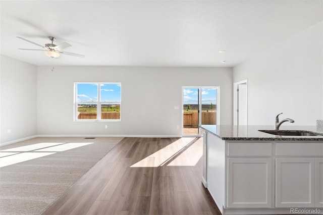 kitchen with white cabinets, sink, light hardwood / wood-style flooring, ceiling fan, and dark stone countertops