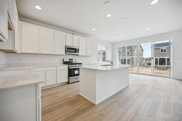 kitchen featuring white cabinets, sink, light hardwood / wood-style flooring, an island with sink, and appliances with stainless steel finishes