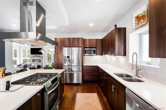 kitchen featuring stainless steel appliances, island exhaust hood, a sink, dark wood-type flooring, and light countertops