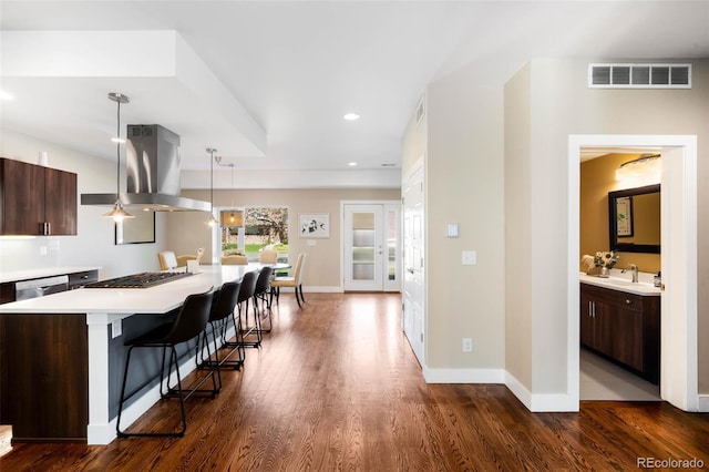 kitchen with island range hood, gas cooktop, light countertops, a kitchen bar, and dark wood-style floors