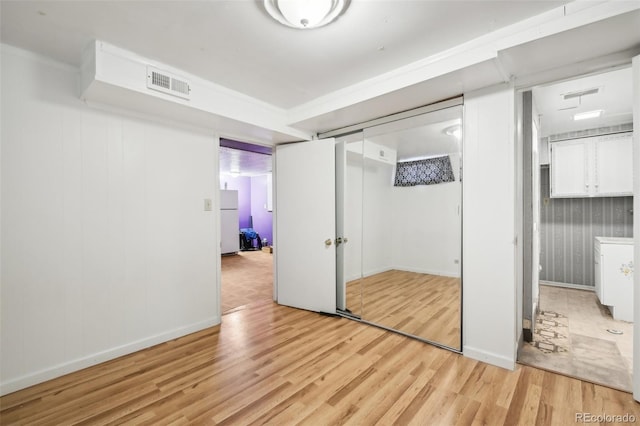 unfurnished bedroom featuring light hardwood / wood-style flooring, a closet, and white refrigerator