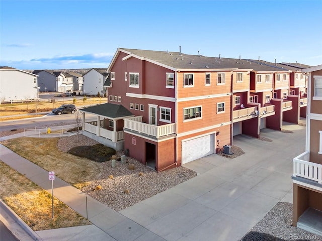 view of building exterior featuring concrete driveway, an attached garage, central AC unit, and a residential view