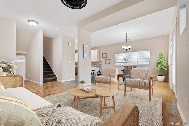 living room with stairs, an inviting chandelier, baseboards, and light wood finished floors