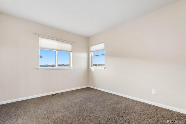 empty room featuring baseboards, visible vents, and dark carpet