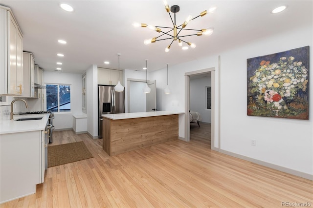 kitchen with light hardwood / wood-style flooring, decorative light fixtures, stainless steel fridge, sink, and white cabinets