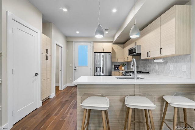 kitchen with light brown cabinets, kitchen peninsula, dark wood-type flooring, appliances with stainless steel finishes, and a breakfast bar