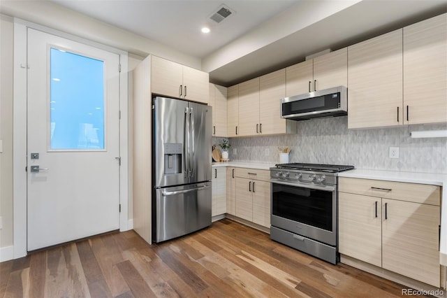 kitchen featuring light brown cabinetry, appliances with stainless steel finishes, dark wood-type flooring, and tasteful backsplash