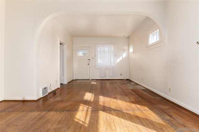 foyer with arched walkways, wood-type flooring, visible vents, and baseboards