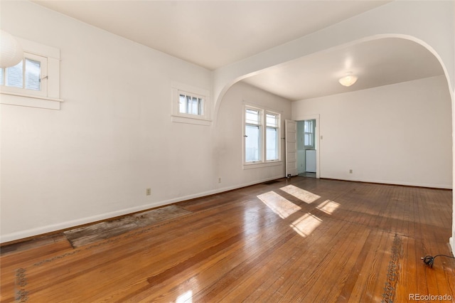 empty room featuring baseboards, arched walkways, and hardwood / wood-style floors