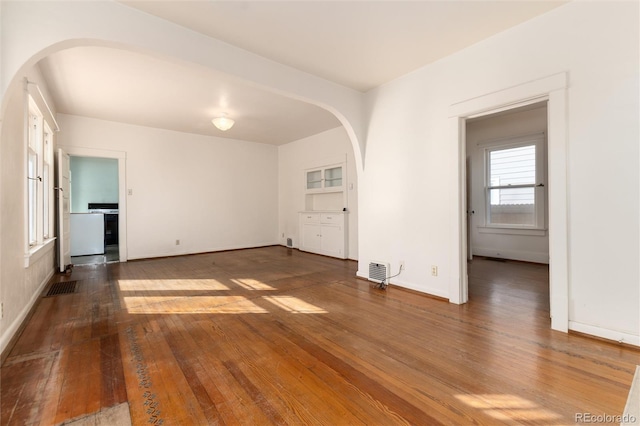 empty room with arched walkways, baseboards, visible vents, and hardwood / wood-style floors