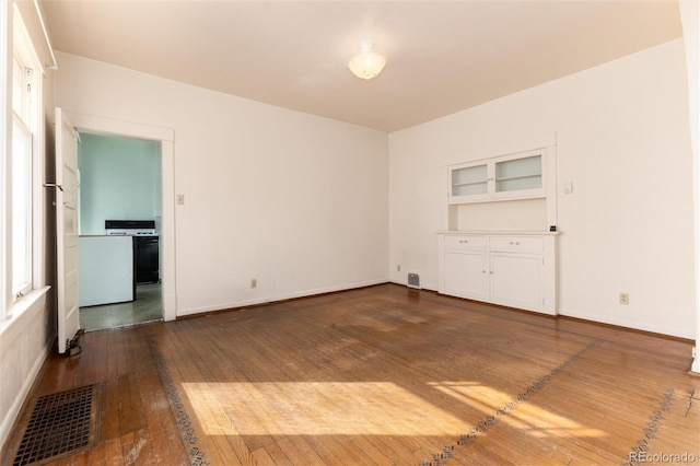 spare room featuring built in features, dark wood-style flooring, visible vents, and baseboards