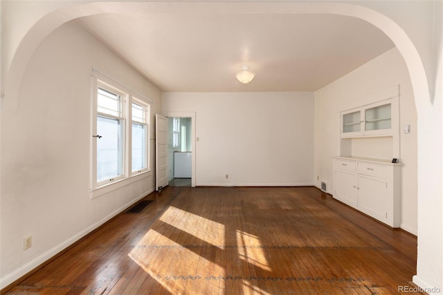 empty room with baseboards, built in shelves, visible vents, and dark wood-style flooring