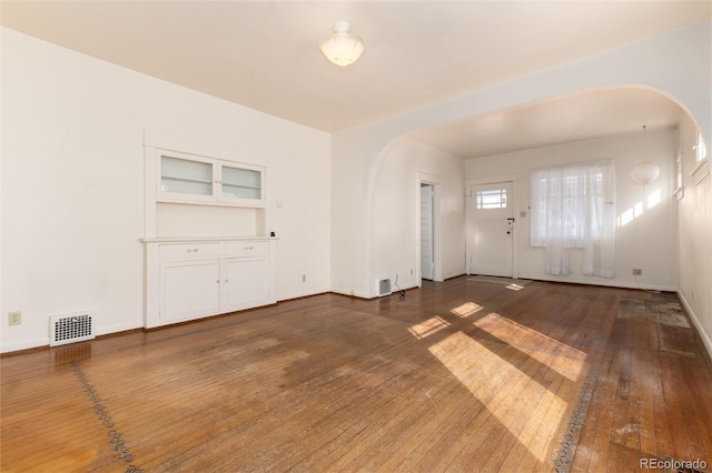 interior space with arched walkways, wood-type flooring, visible vents, and baseboards